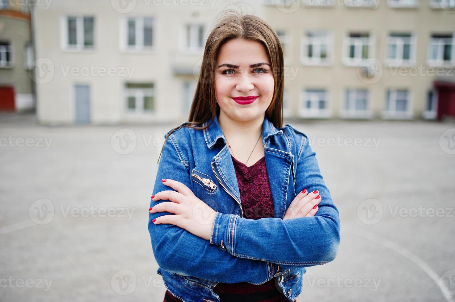 giovane adolescente paffuta indossare su abito rosso e giacca di jeans poste contro il cortile della scuola. foto