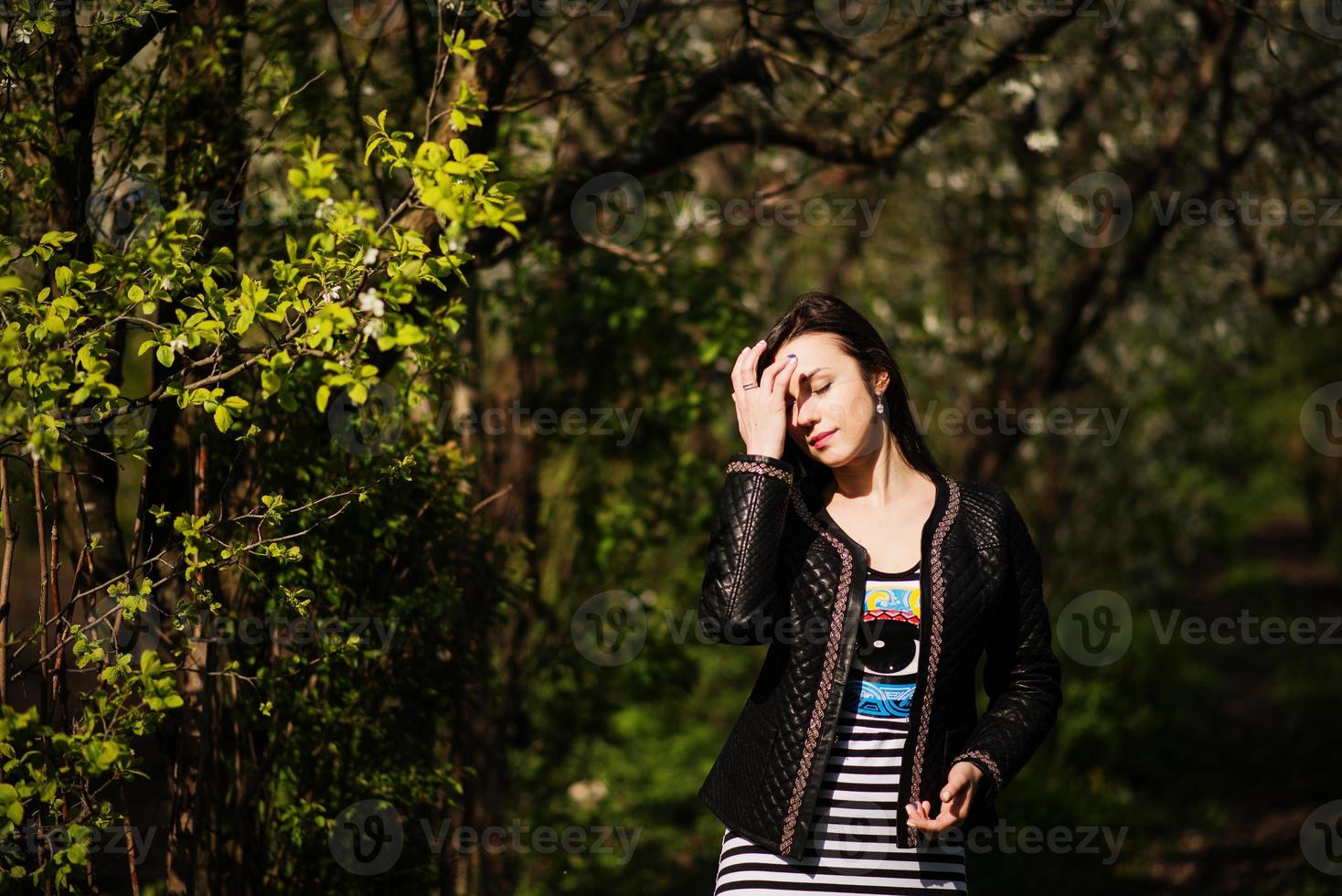 ragazza bruna in giacca di pelle poste sul giardino di primavera. camminare alla luce del sole. foto