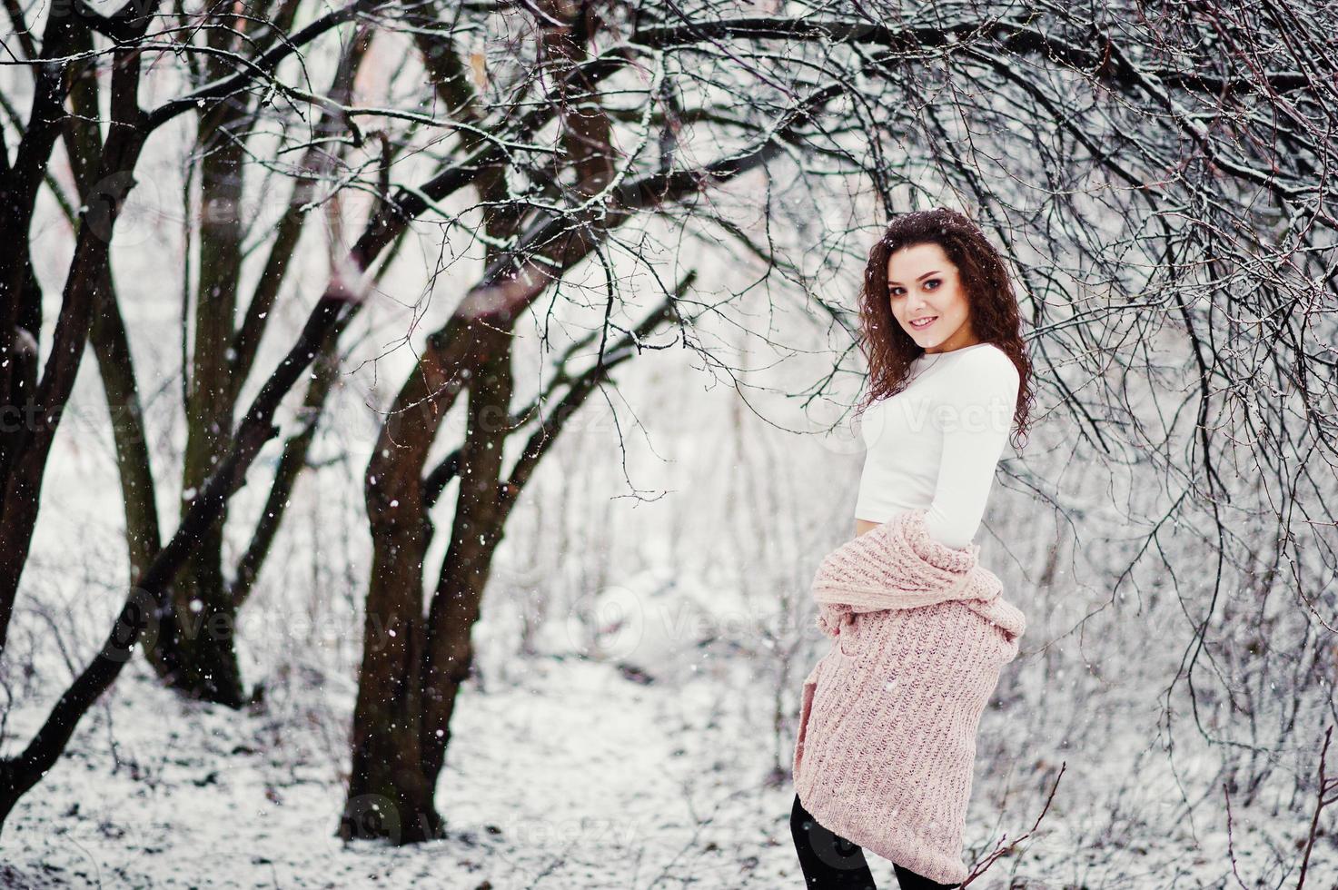 sfondo ragazza bruna riccia neve che cade, indossare un maglione caldo lavorato a maglia, minigonna nera e calze di lana. modello in inverno. ritratto di moda con tempo nevoso. foto dai toni di instagram.