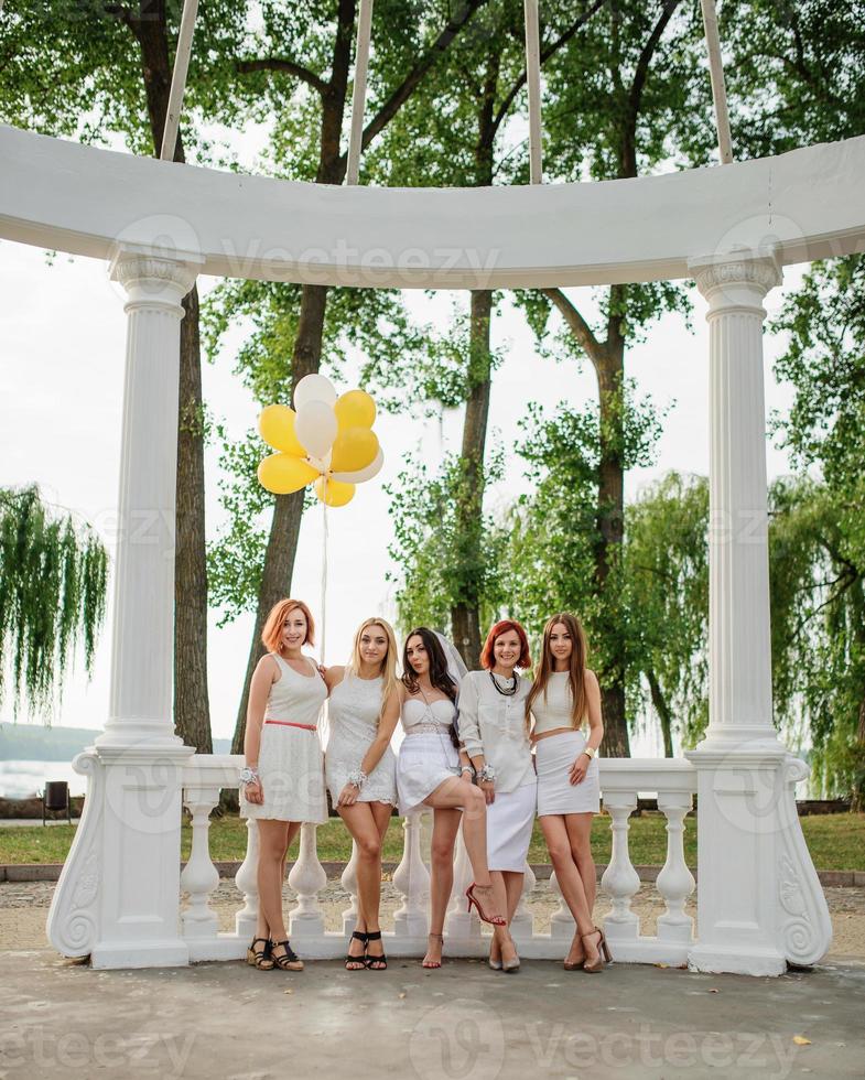 cinque ragazze con palloncini a portata di mano indossate su abiti bianchi ad addio al nubilato contro colonne bianche di arch. foto