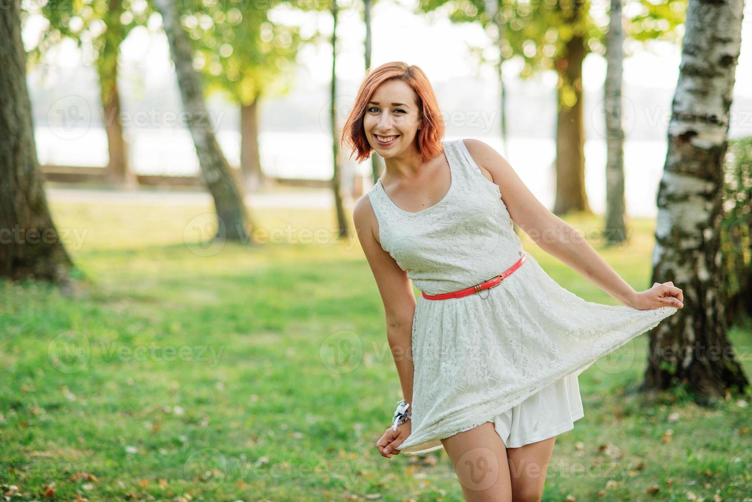 Ritratto di ragazza dai capelli rossi che indossa un abito bianco contro il parco alla festa di addio al nubilato. foto