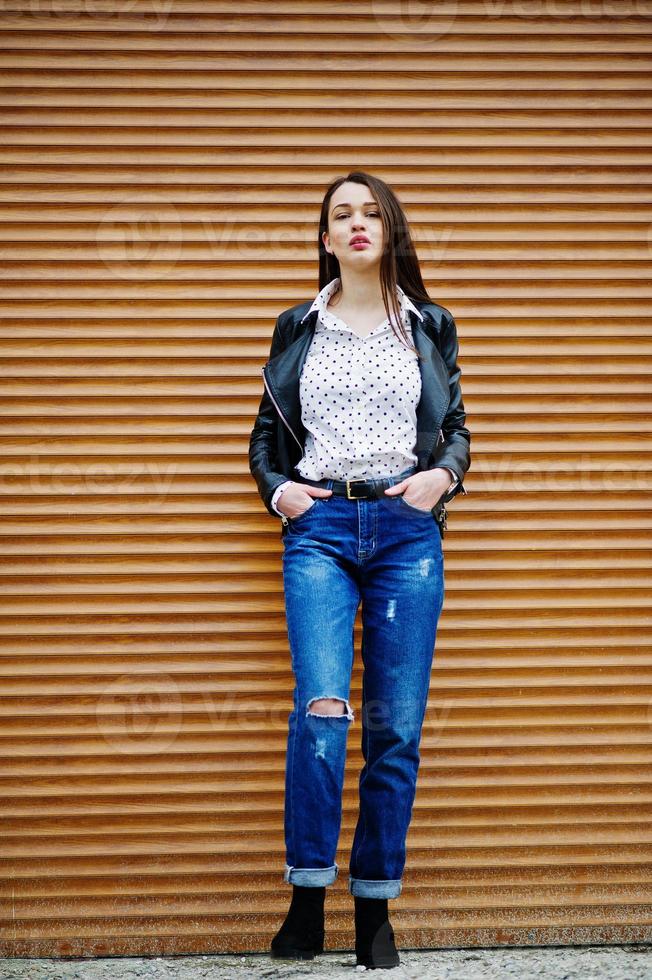 ritratto a figura intera di giovane ragazza alla moda indossare su giacca di pelle e jeans strappati texture di sfondo dell'otturatore. stile modello di moda di strada. foto