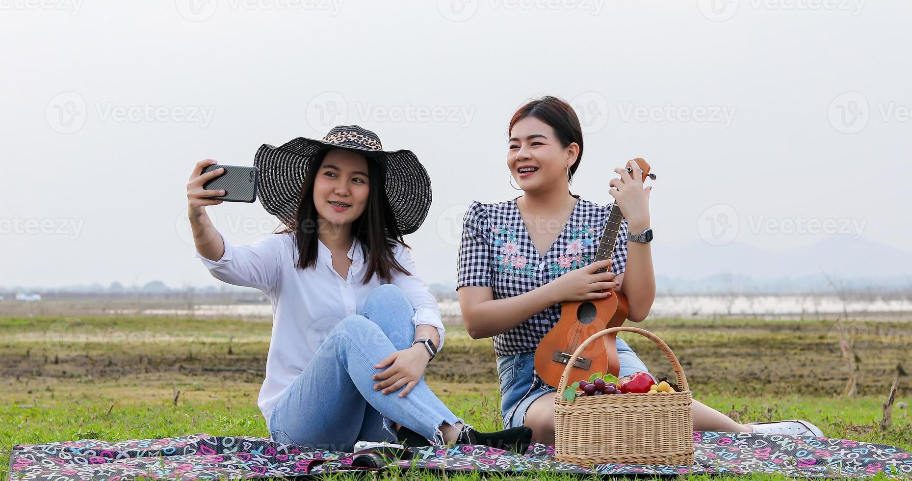 un gruppo di amici asiatici che giocano a ukelele e trascorrono del tempo a fare un picnic durante le vacanze estive. sono felici e si fanno selfie, si rilassano durante il viaggio di concetto di vacanza foto