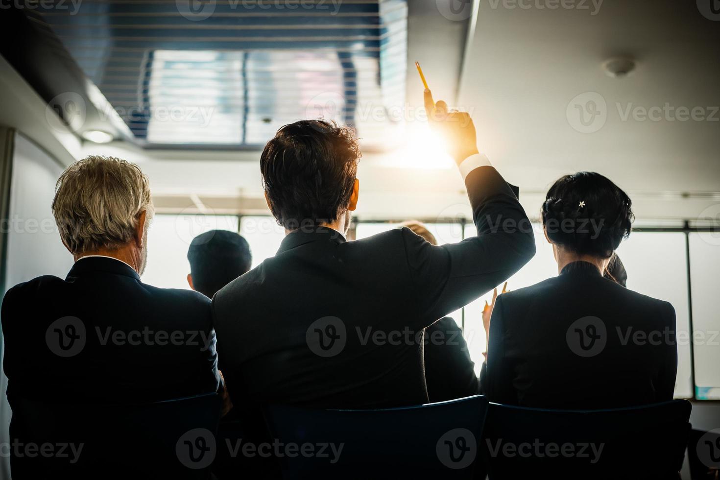 pubblico aziendale alzando la mano mentre l'uomo d'affari sta parlando in formazione per l'opinione con il leader della riunione nella sala conferenze foto