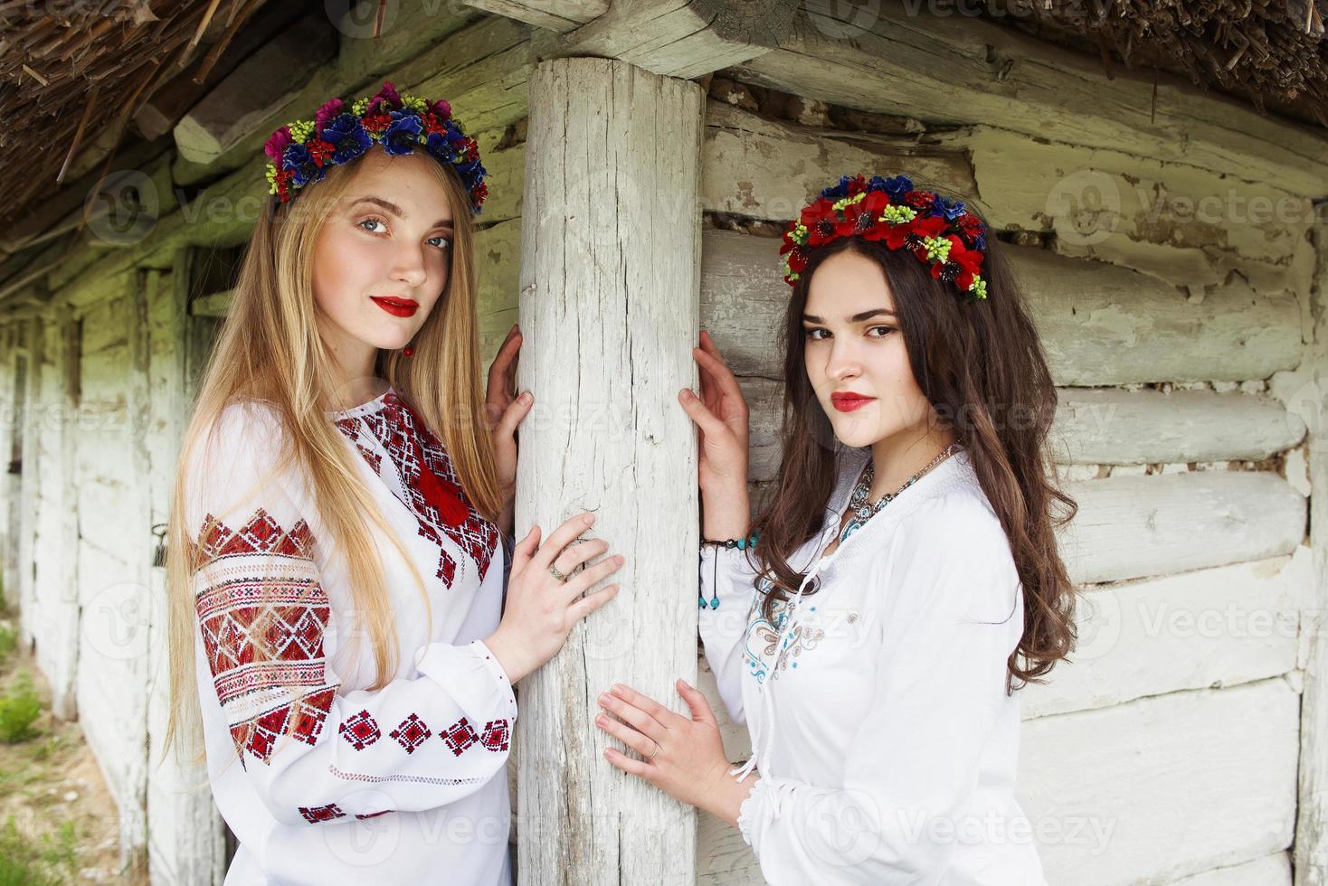 due giovani belle donne con i capelli lunghi in camicette ucraine e in un ghirlande in un villaggio etnico all'aperto a kyiv ucraina foto