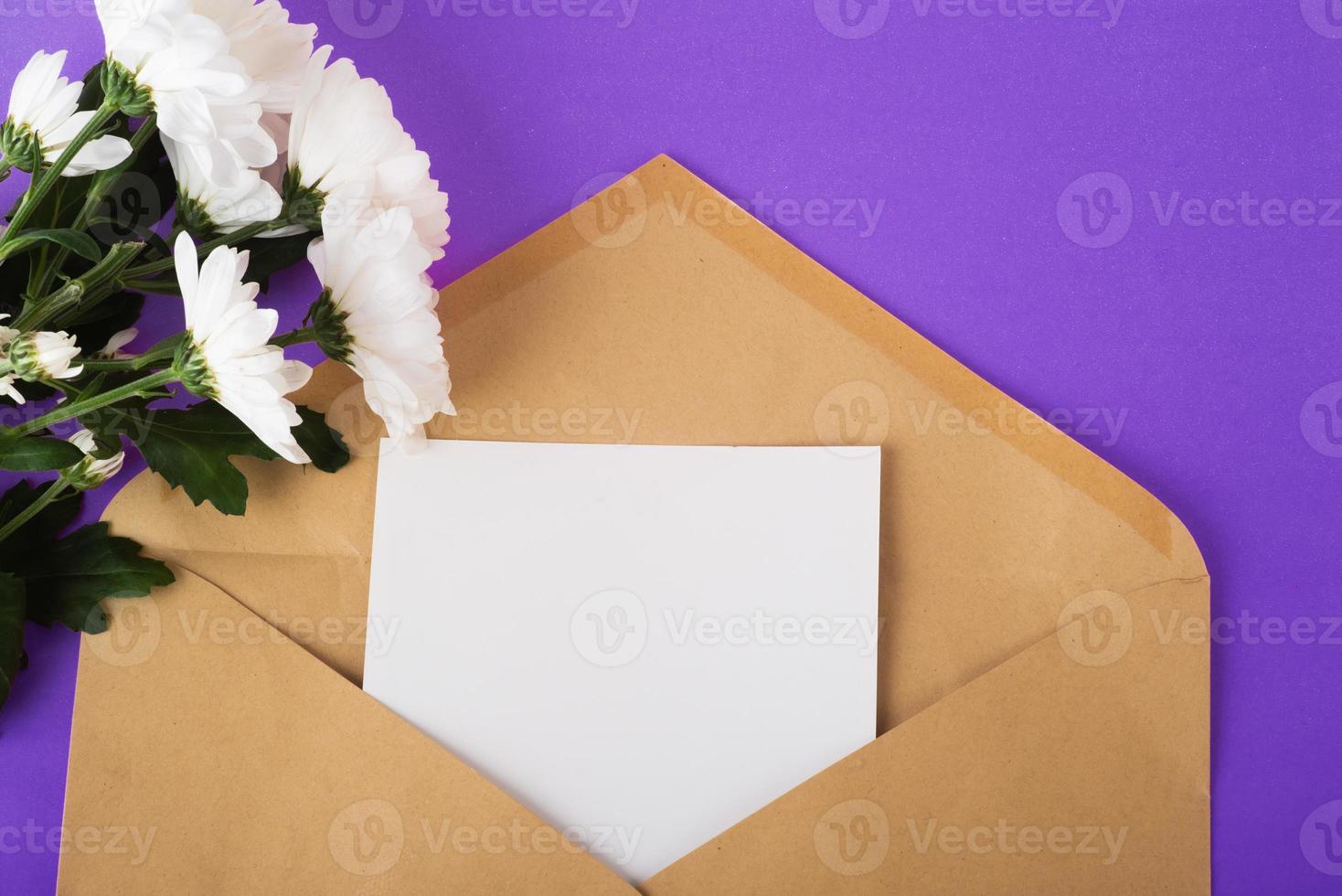 busta di carta artigianale aperta con pezzo di carta vuoto e fiori bianchi vicino su sfondo molto peri foto