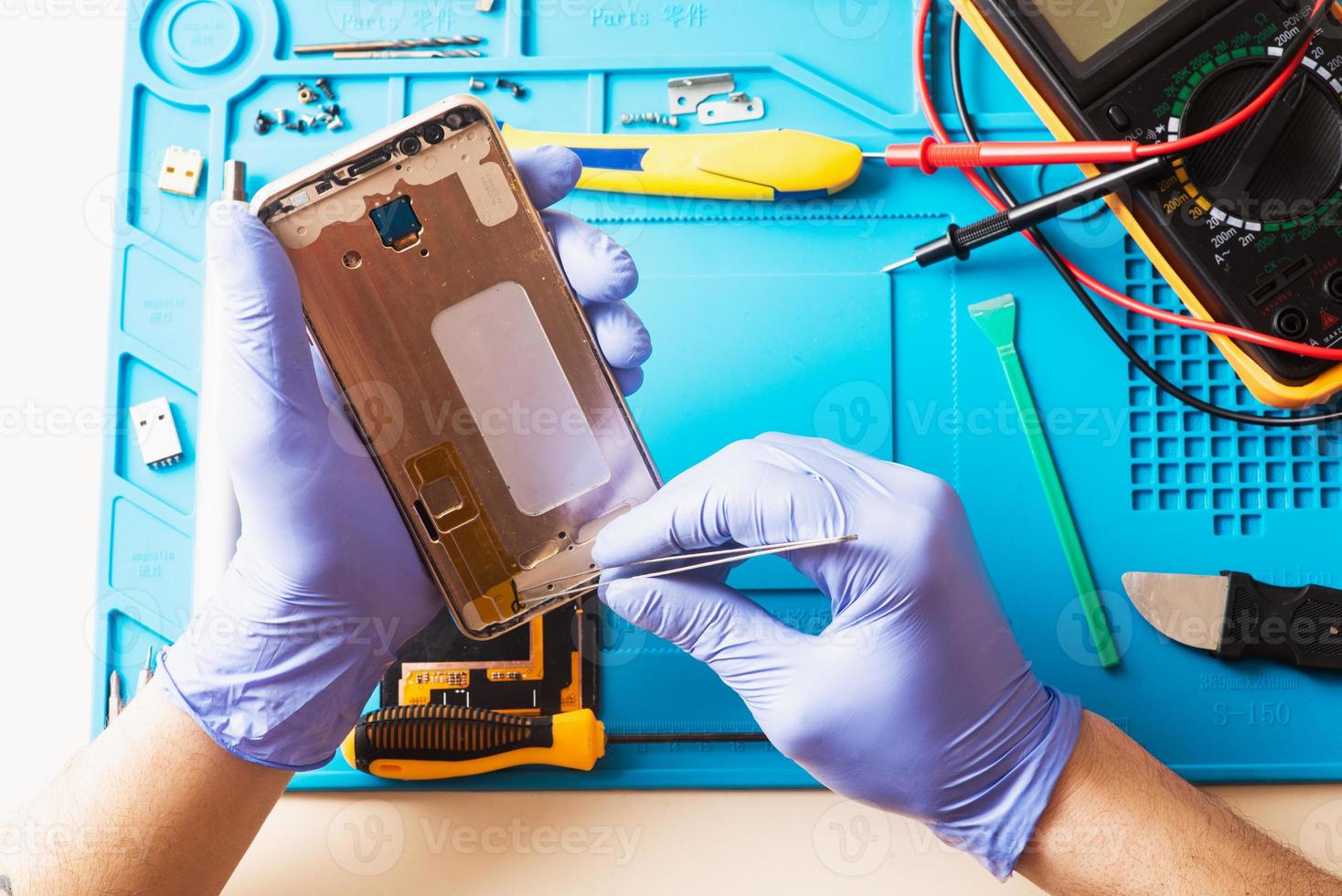 riparazione cellulari. il master telecomanda il cellulare utilizzando gli strumenti su un apposito tappetino. piatto laico, vista dall'alto foto