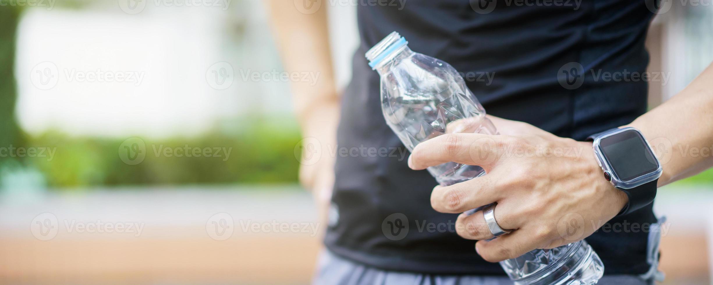 sportivo asiatico attivo che si rilassa e beve un'acqua in bottiglia dopo la corsa o l'allenamento all'aperto. l'uomo asiatico beve un'acqua durante la pausa dall'esercizio. un uomo sano che si impegna per l'allenamento cardio. foto