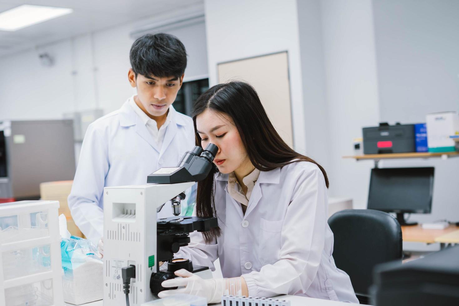 due scienziati medici che lavorano in laboratorio medico, giovane scienziata che guarda al microscopio. selezionare il focus in una giovane scienziata foto