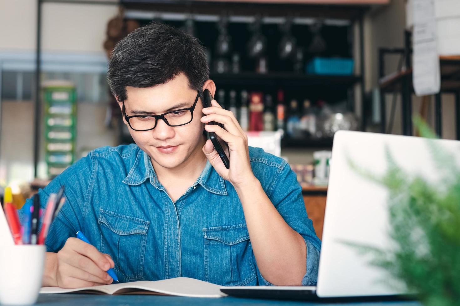 i giovani uomini asiatici rispondono al telefono felici dopo il nuovo ordine del cliente, dell'imprenditore che lavora a casa, imballando l'ufficio in background, e-commerce di shopping online o concetto di lavoro freelance. foto