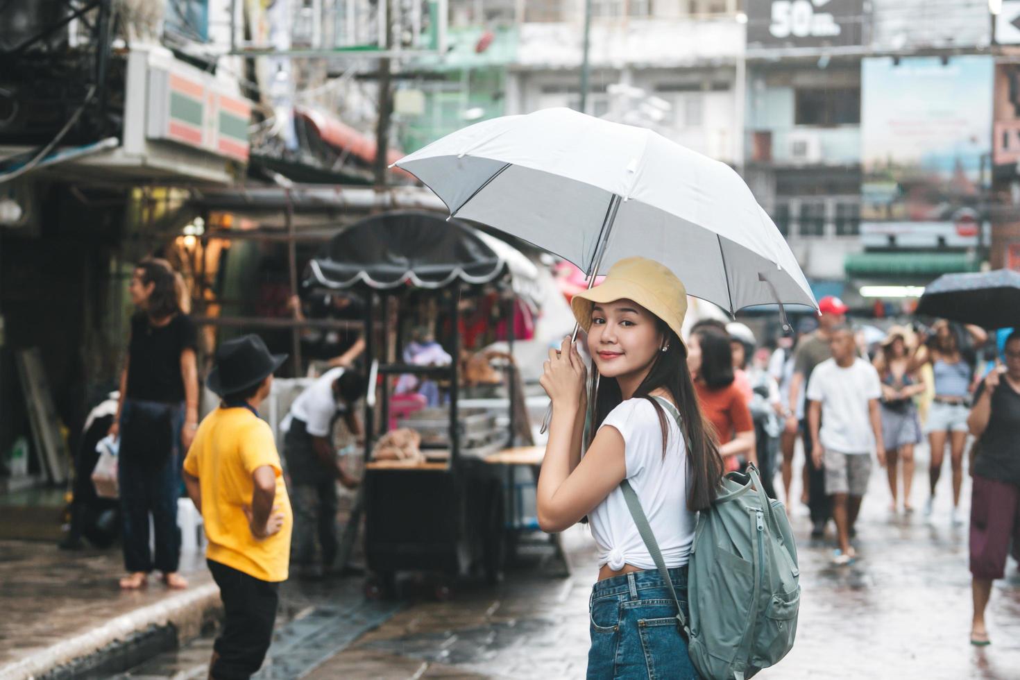 il giovane viaggiatore asiatico adulto tiene l'ombrello quando piove in una strada pedonale. foto