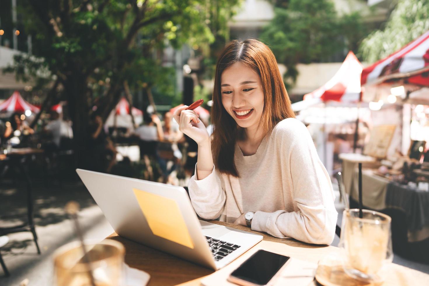 libero professionista di affari donna asiatica adulta che utilizza il computer portatile per lavorare al caffè sul marciapiede foto