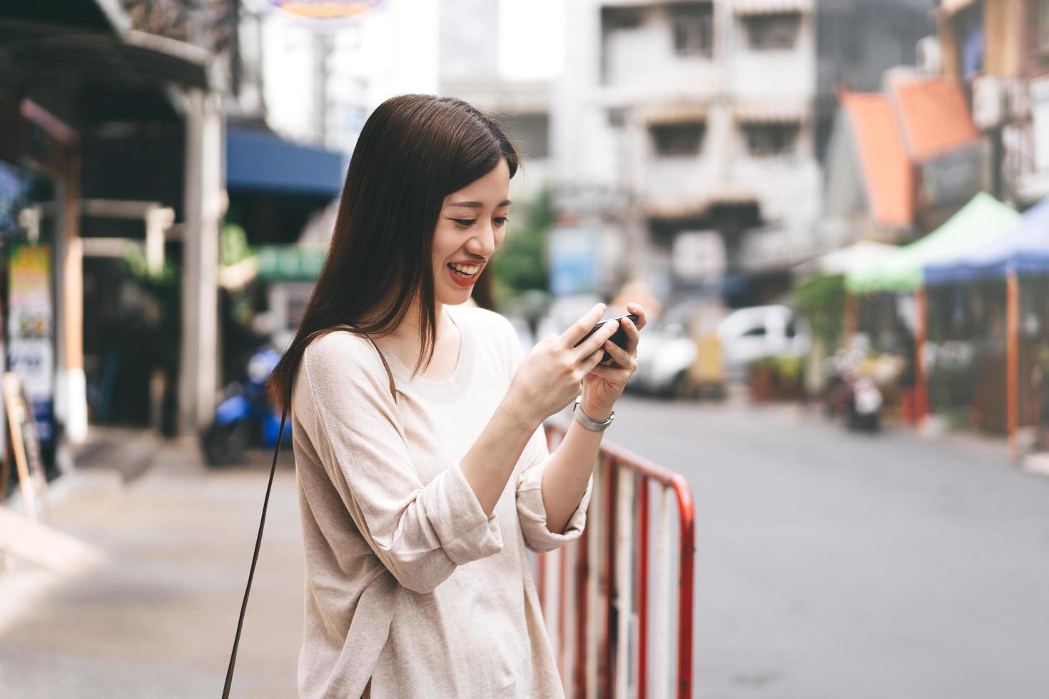 femmina asiatica adulta che tiene telefono cellulare per giocare all'aperto in città. foto