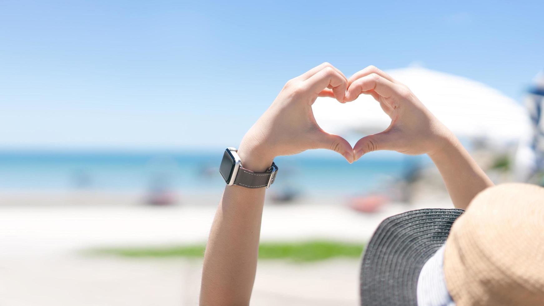 retrovisione della mano asiatica della donna del viaggiatore con il gesto del cuore per amore. foto