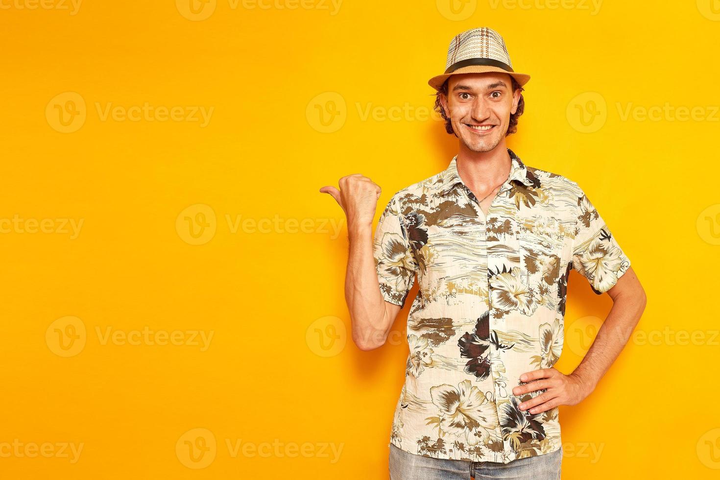 un viaggiatore turistico maschio sorridente felice in vacanza punta il pollice in un'area vuota per la pubblicità. isolato su uno sfondo giallo con spazio per il testo. concetto - persone, avventure, voli all'estero foto