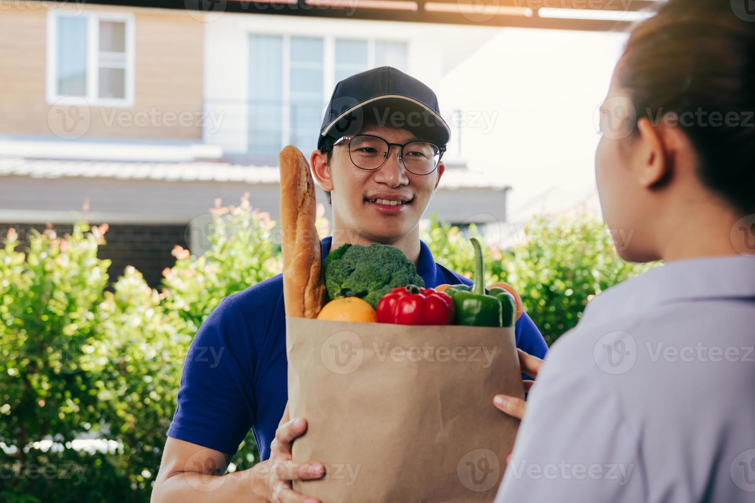 uomo asiatico di consegna che consegna un sacchetto di carta all'interno con verdure o cibo a una donna asiatica davanti a casa sua. foto