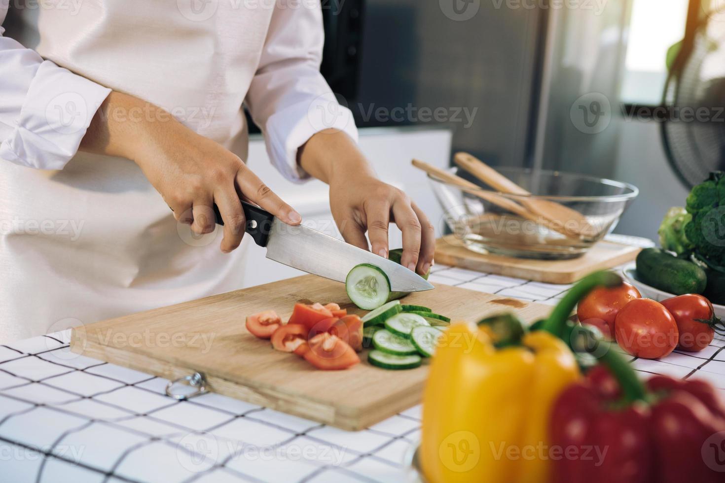 donna che usa coltello e mani che tagliano il cetriolo su tavola di legno nella stanza della cucina. foto