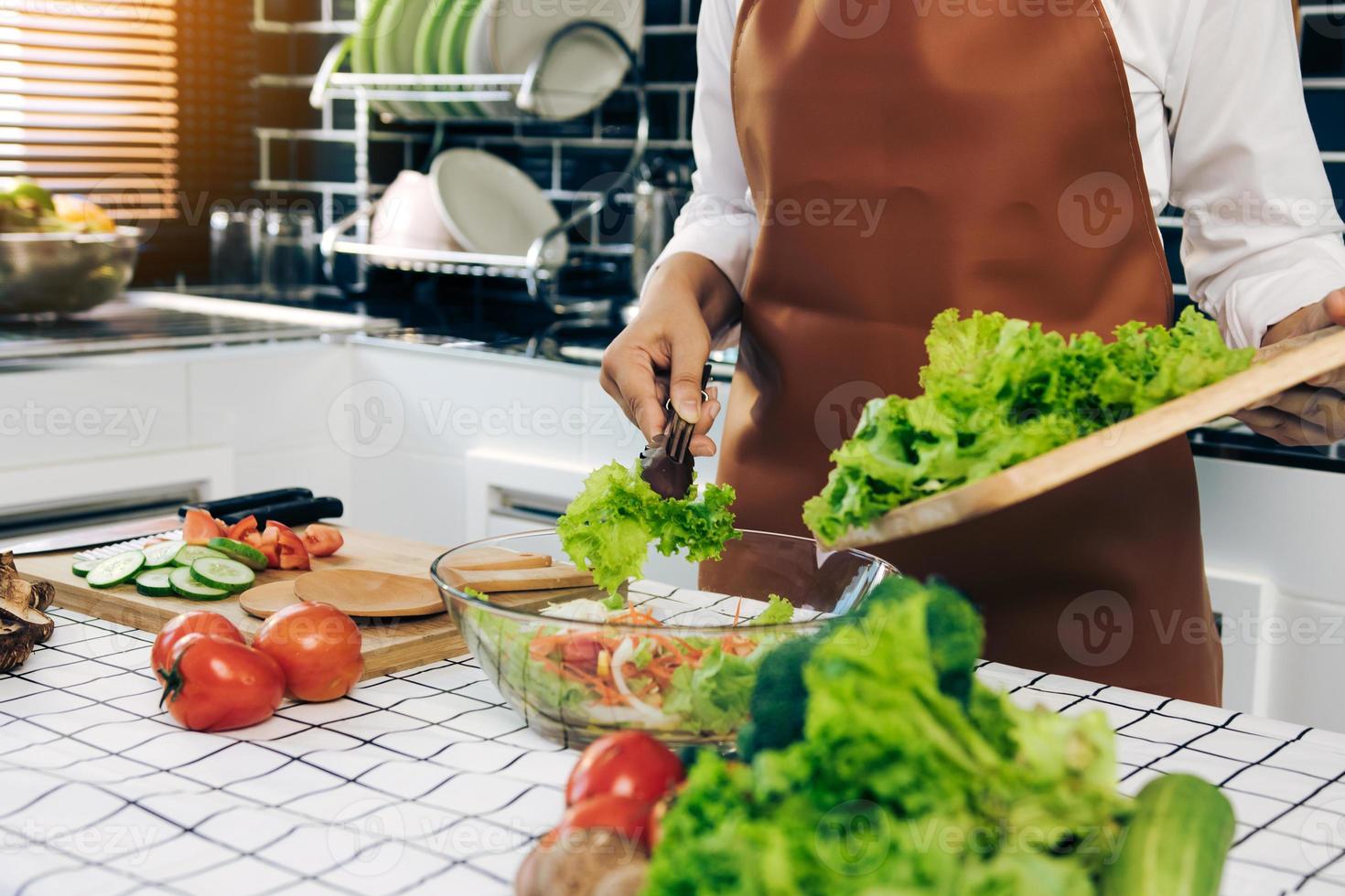 la donna asiatica sta usando le pinze per prendere l'insalata sul tagliere di legno sulla tazza di insalata nella stanza della cucina. foto