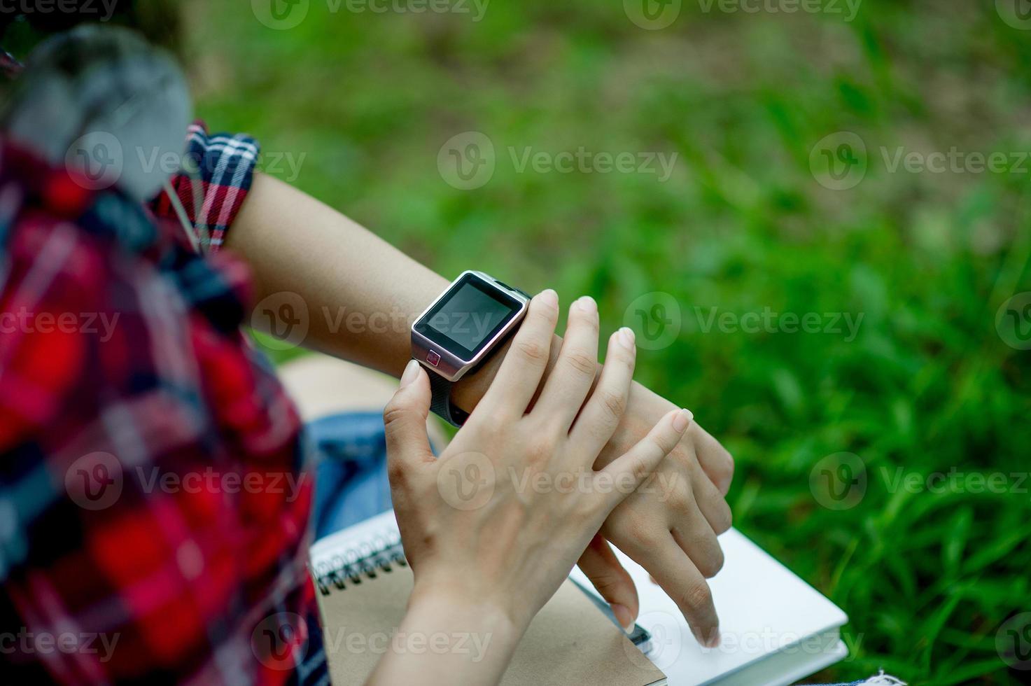 la ragazza guarda l'orologio in mano, guarda l'ora con un orologio nero, indossa una maglietta rossa e uno sfondo verde. e c'è uno spazio di copia. foto