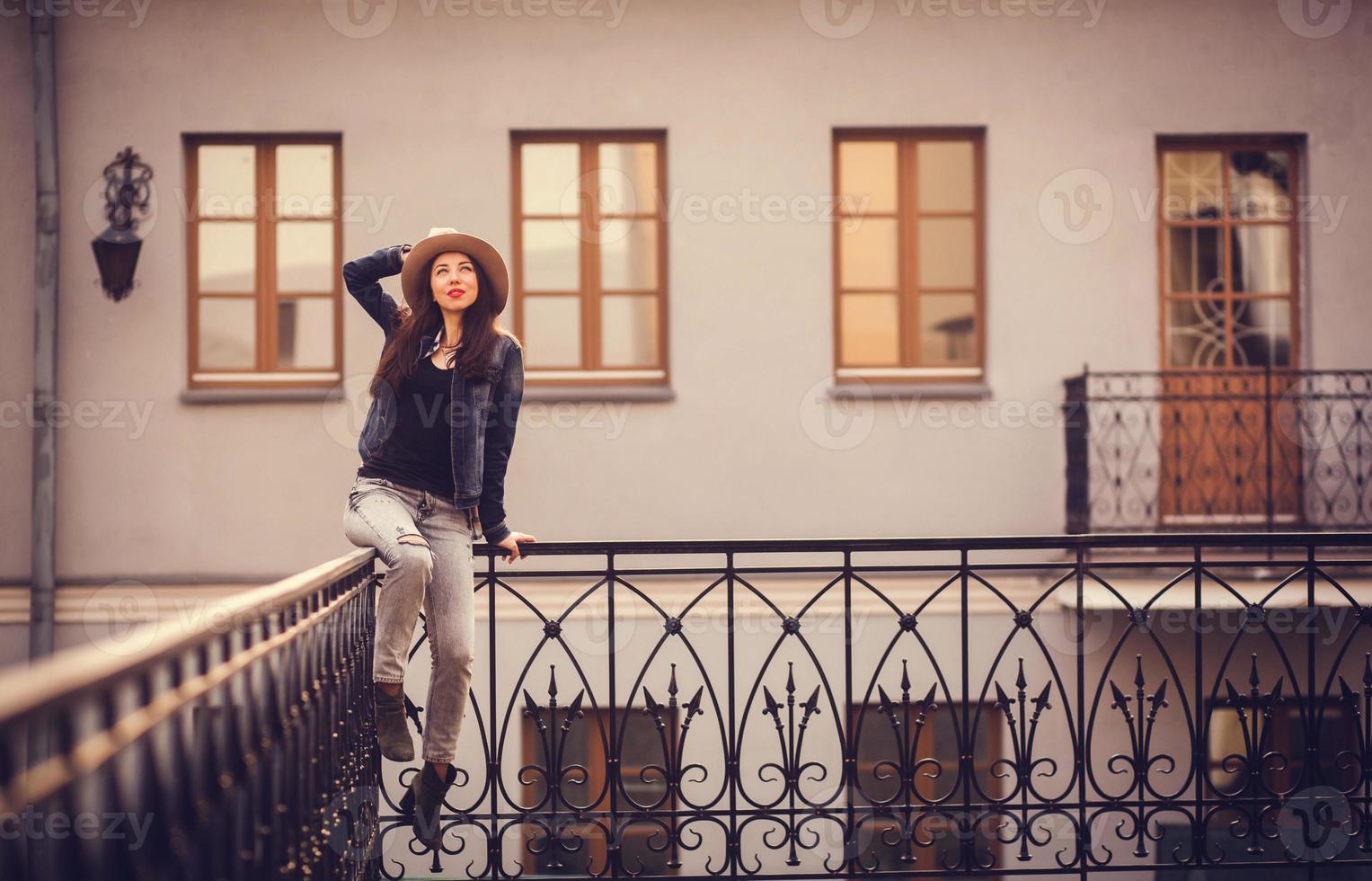 bella ragazza con un cappello seduto su una ringhiera in città foto