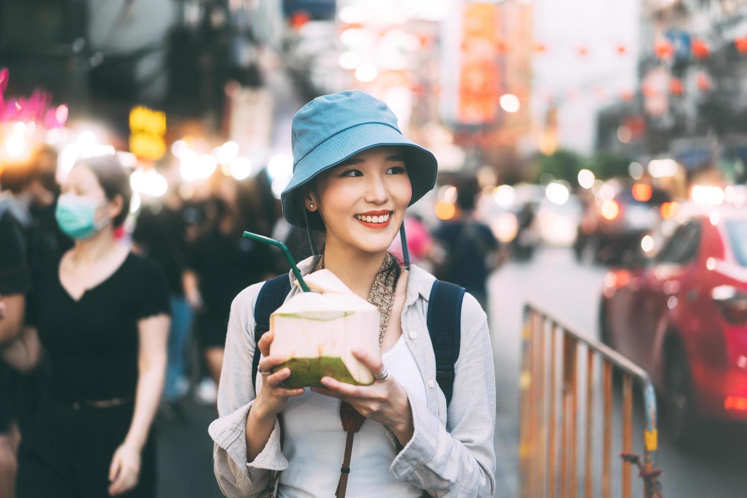 giovane adulto asiatico foodie donna zaino viaggiatore mangiare succo di cocco al cibo di strada della città cinese. foto