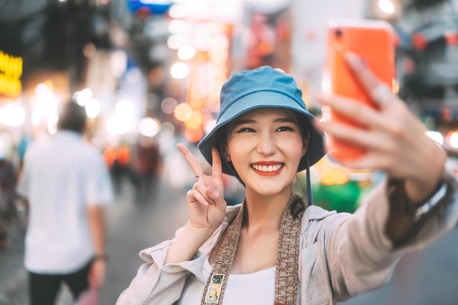giovane adulto asiatico donna viaggiatore selfie con cellulare indossare zaino chinatown street food market backgprund. foto