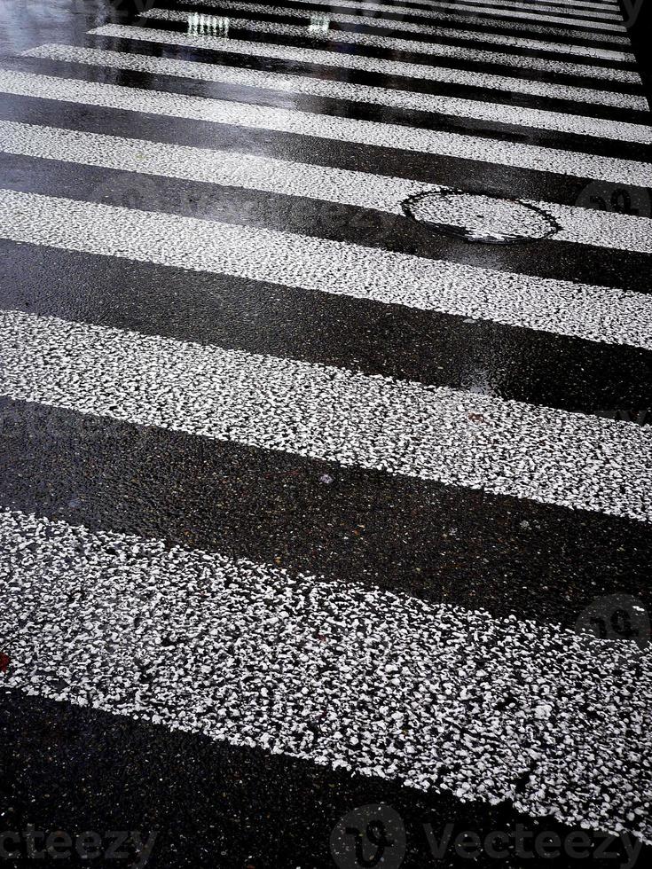 strada asfaltata bagnata con strisce bianche di strisce pedonali. foto