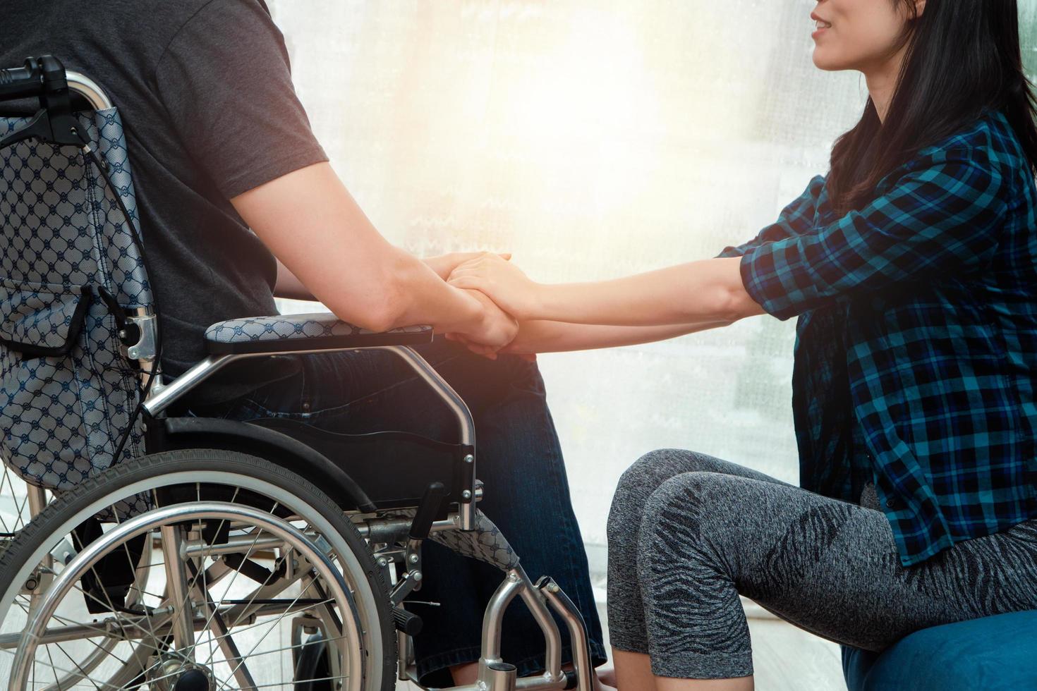 un uomo asiatico su una sedia a rotelle in casa dopo un incidente d'auto e sua moglie per incoraggiare. il concetto di assistenza reciproca e nuove tecnologie ha reso le persone con disabilità uguaglianza nella società. foto