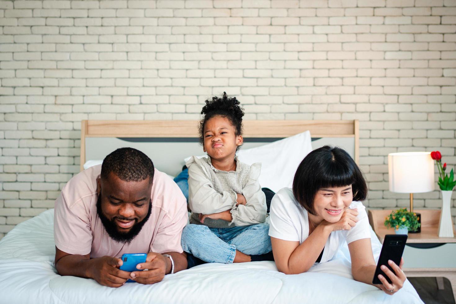 le ragazze afroamericane non sono soddisfatte e tristi, sedute in mezzo tra padre e madre. i genitori usano lo smartphone e i bambini abbandonati. i bambini hanno bisogno dell'attenzione dei genitori. foto