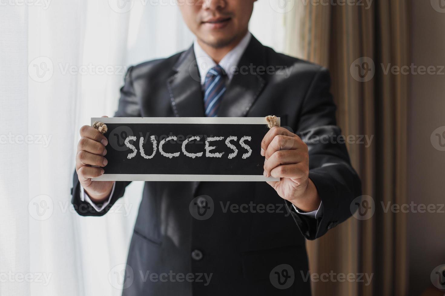 colpo ritagliato di uomo d'affari in abito nero e cravatta con cartello di successo foto