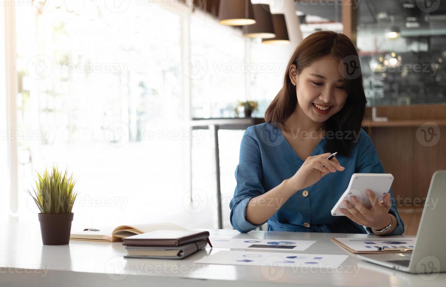 donna asiatica di affari che utilizza la calcolatrice per fare la finanza di matematica sulla scrivania di legno in ufficio, tasse, contabilità, concetto finanziario foto