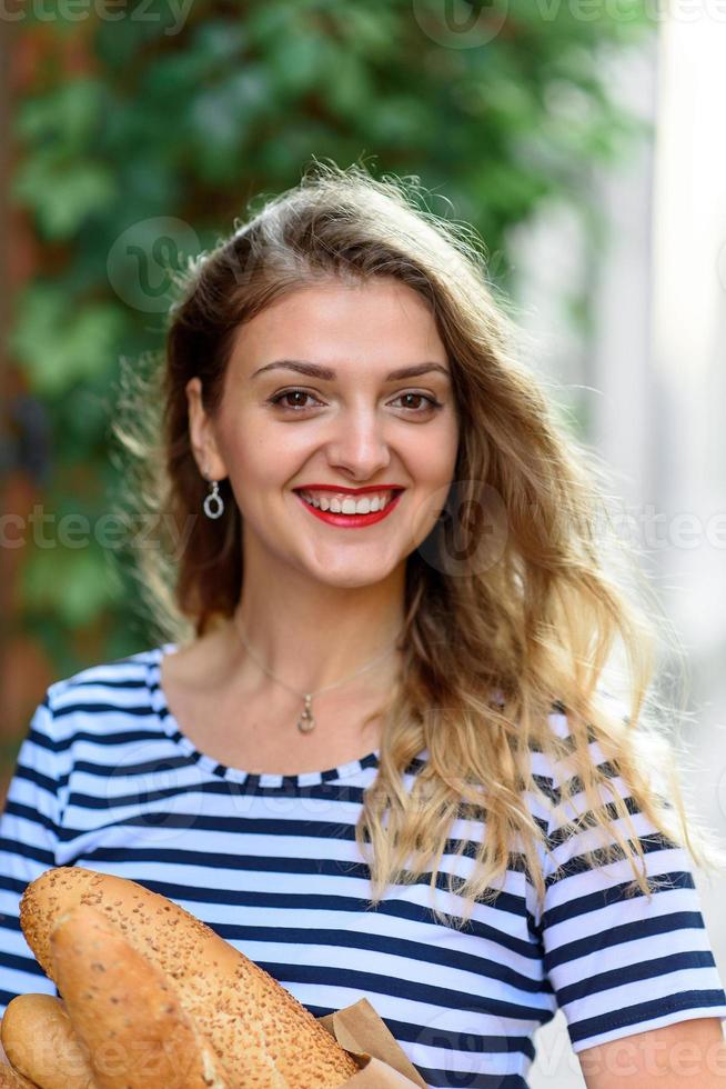 giovane bella donna in posa con una baguette in mano per le strade della francia. foto