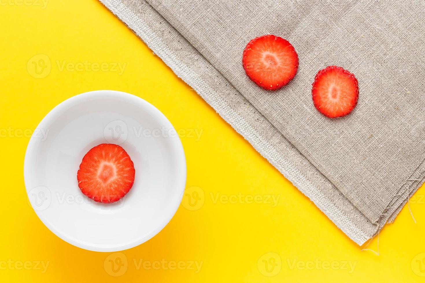 tre fette di fragole fresche in un piatto bianco rotondo su sfondo giallo e tela di sacco. immagine orizzontale vista dall'alto. foto