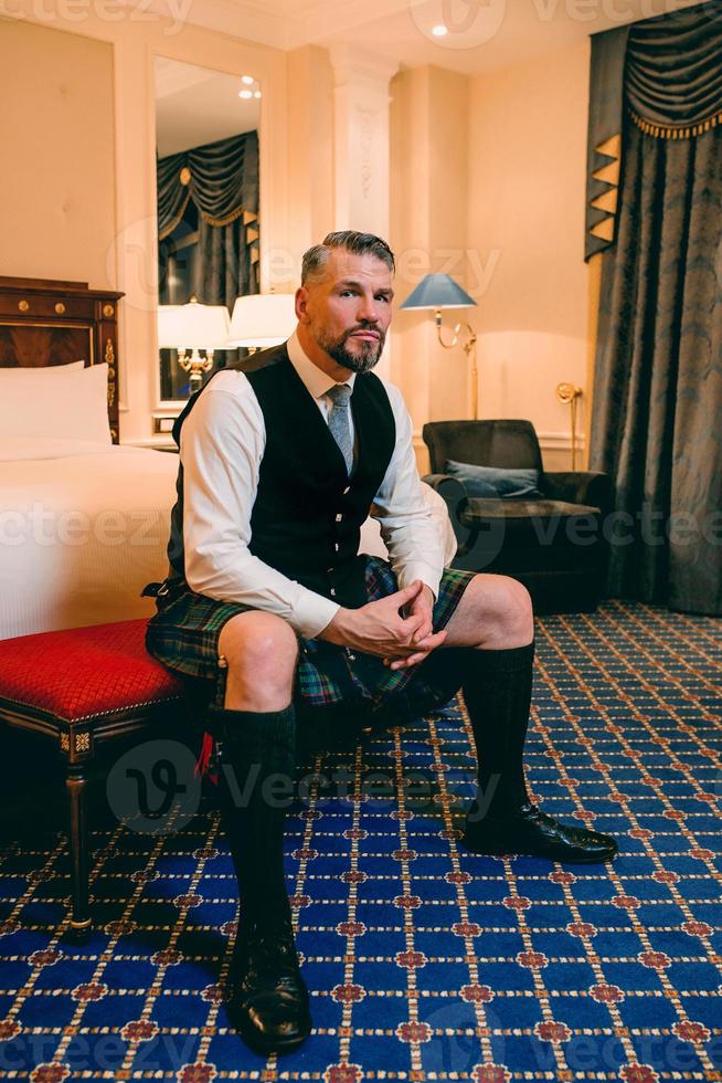 bel uomo maturo coraggioso ed elegante scozzese in kilt in una camera d'albergo elegante. stile, moda, stile di vita, cultura, viaggi, concetto etnico. foto