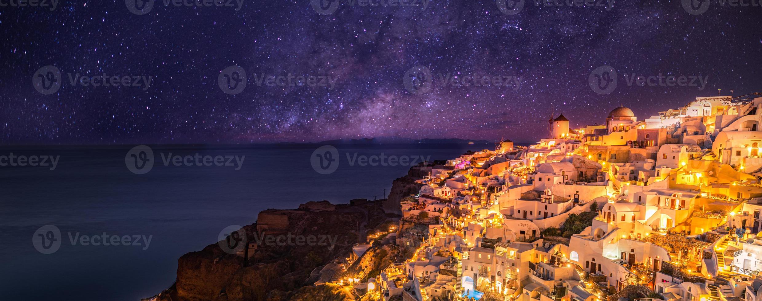 villaggio di oia alla luce del tramonto con le stelle e la via lattea, santorini, grecia. incredibile paesaggio per le vacanze estive, architettura bianca e luci serali. famosa destinazione di viaggio, sfondo di viaggio urbano foto