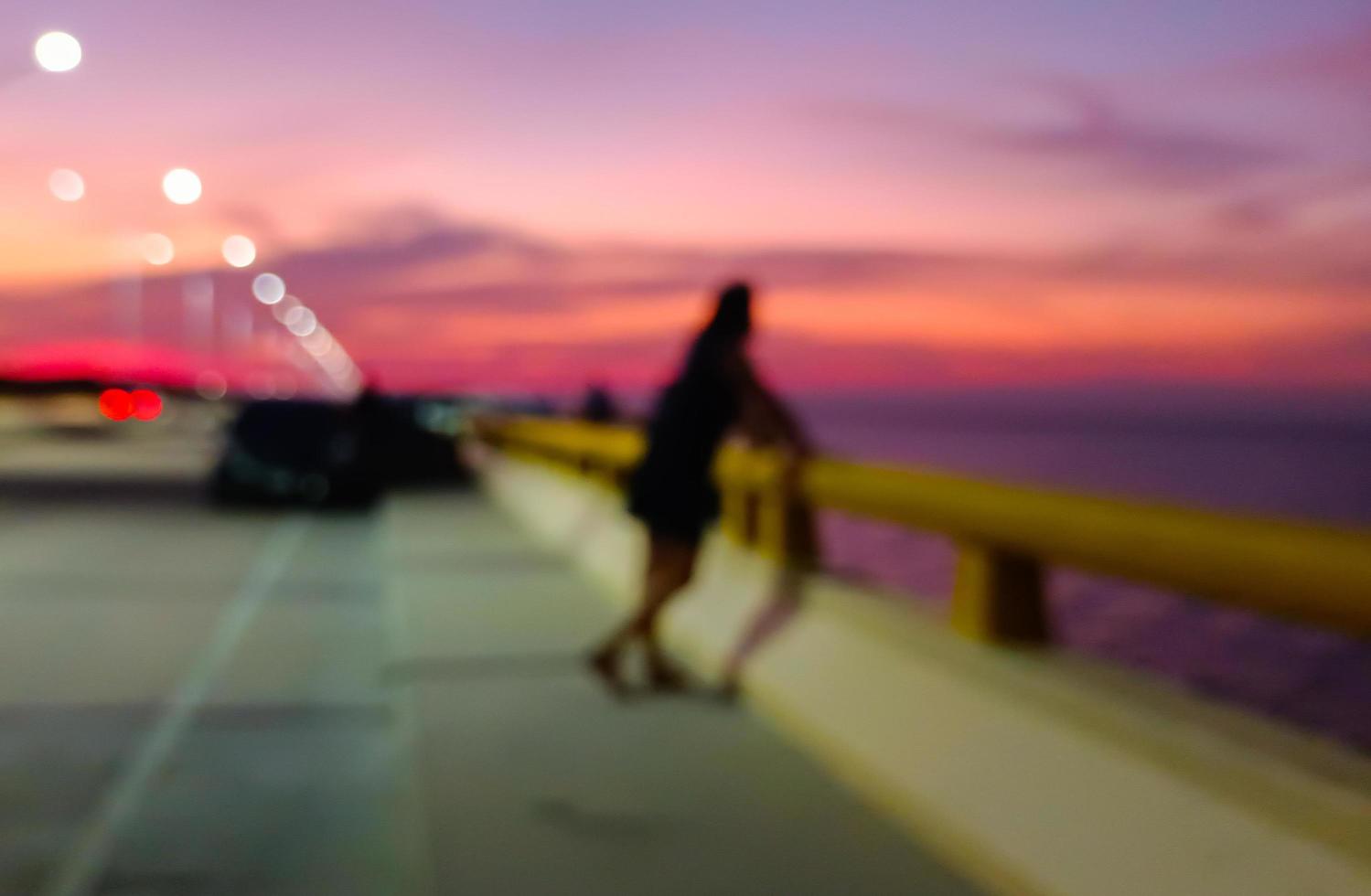 bellissimo sfondo di luci bokeh al crepuscolo, persone in piedi sulle ringhiere del mare che guardano al mare al tramonto. cielo viola foto