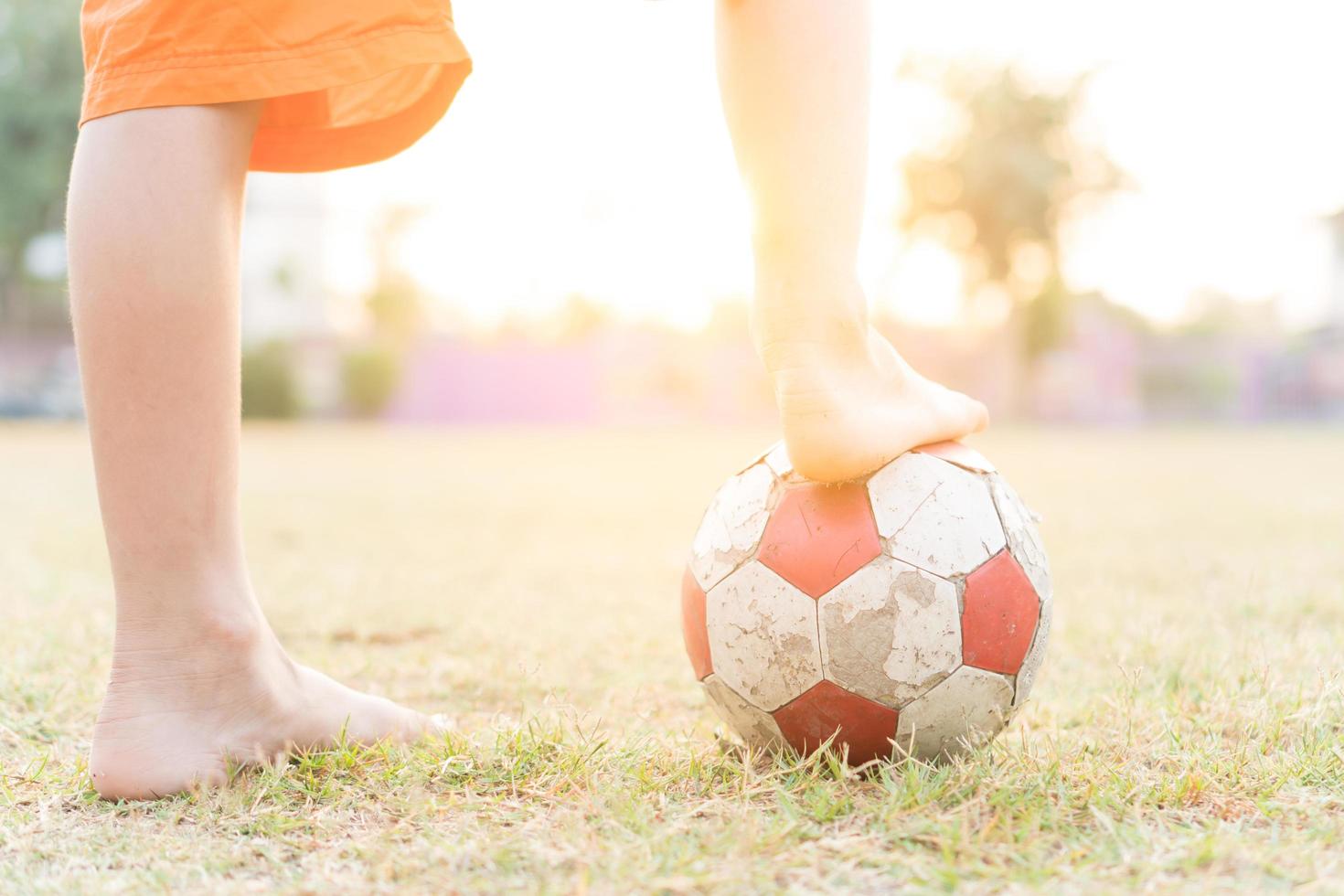 le gambe di un ragazzino con un vecchio pallone da calcio biancorosso al mattino. foto