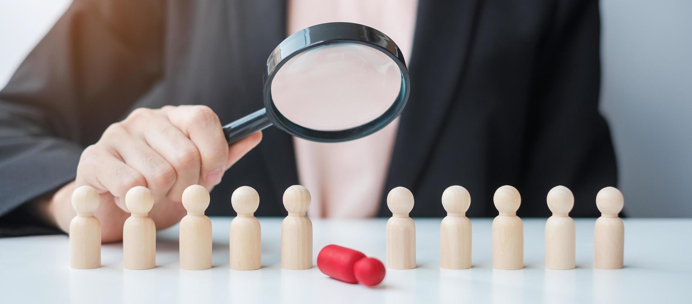 mano della donna d'affari che tiene la lente d'ingrandimento per il reclutamento di leader uomo in legno dalla folla di dipendenti. gestione delle risorse umane, reclutamento, lavoro di squadra, assunzione e concetti di leadership foto