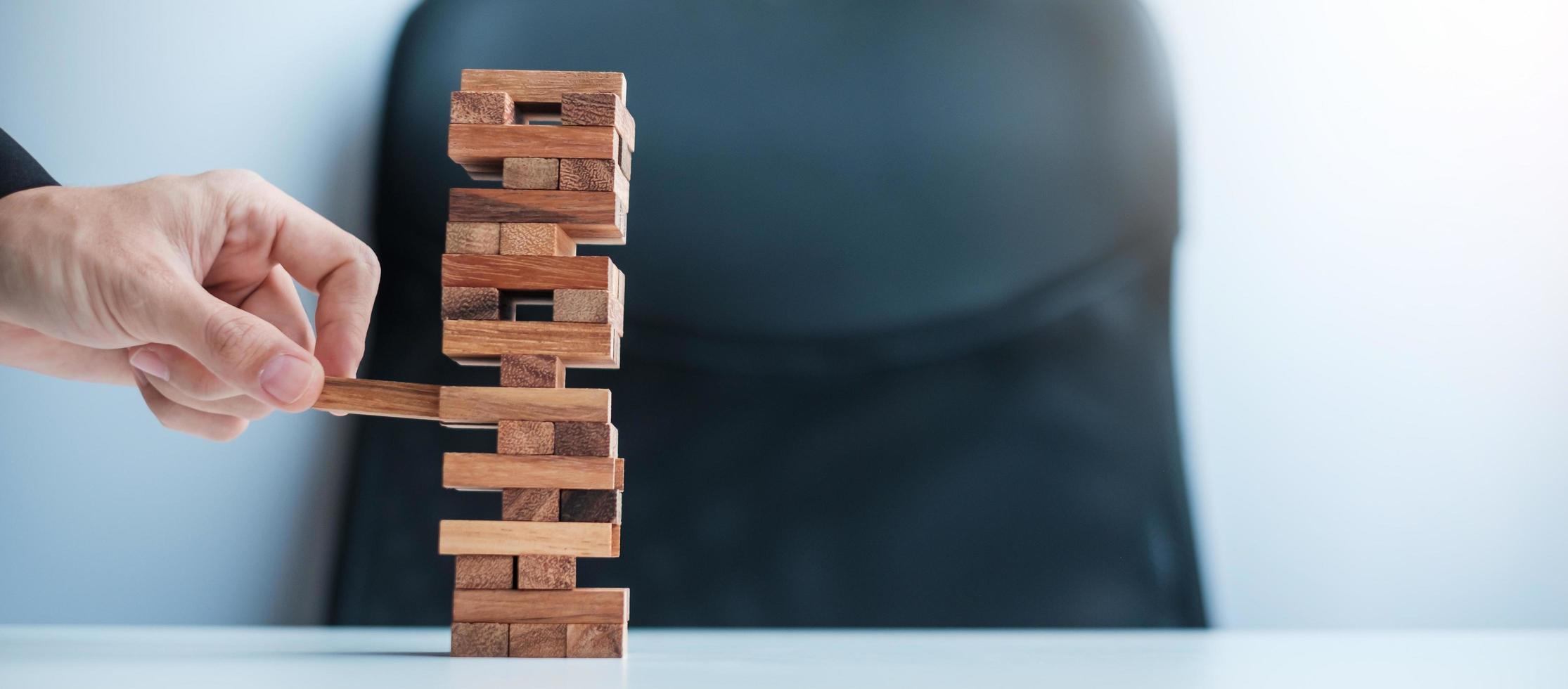 mano dell'uomo d'affari che posiziona o tira il blocco di legno sulla torre. concetti di pianificazione aziendale, gestione del rischio, soluzione e strategia foto