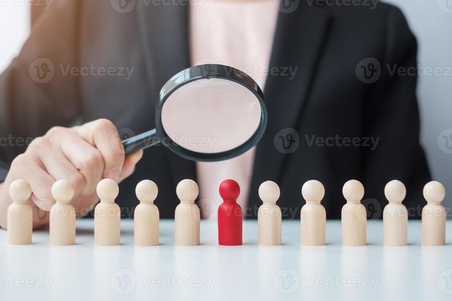 mano della donna d'affari che tiene la lente d'ingrandimento per il reclutamento di leader uomo in legno dalla folla di dipendenti. gestione delle risorse umane, reclutamento, lavoro di squadra, assunzione e concetti di leadership foto