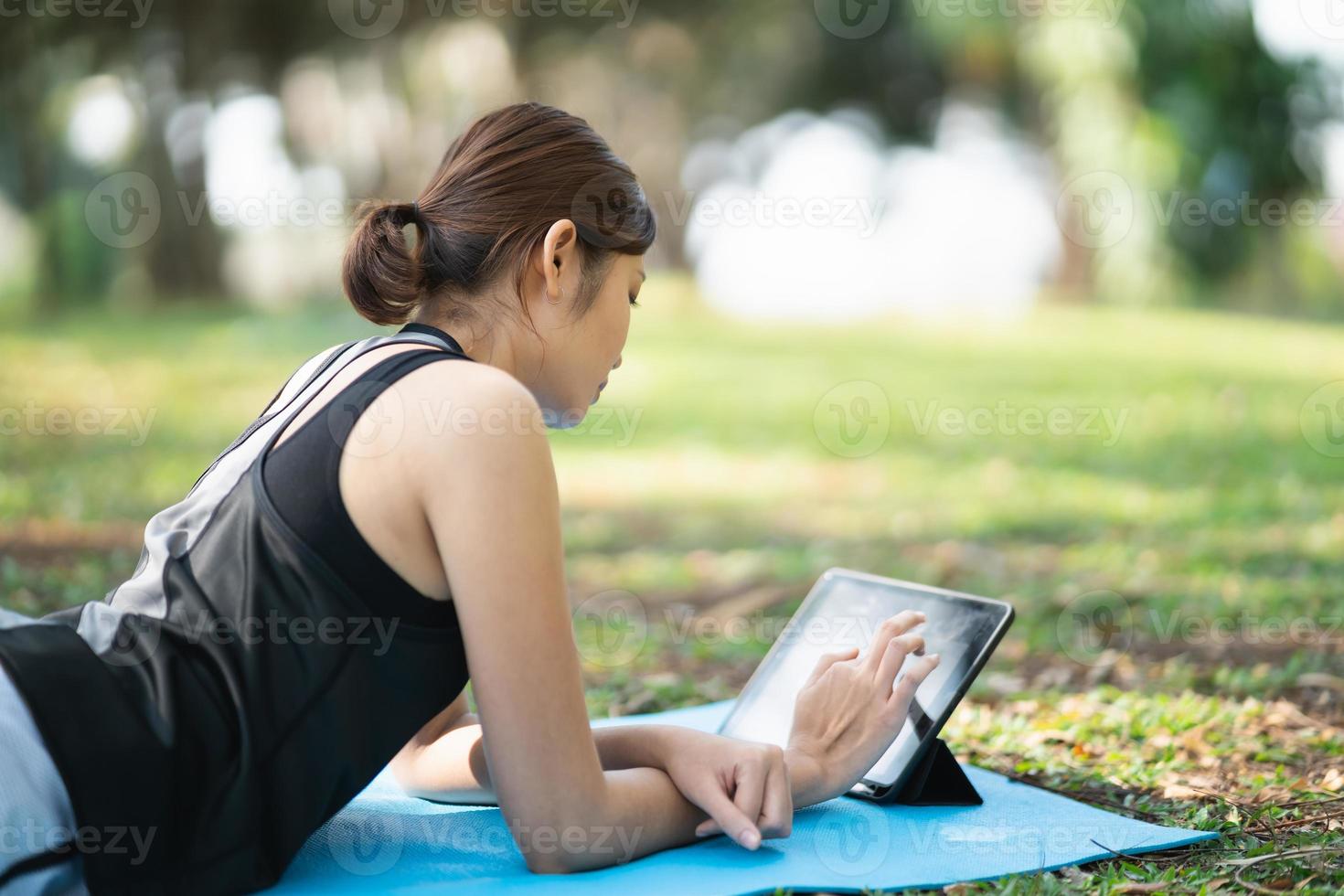 donna asiatica di forma fisica che fa uno yoga secondo un video clip. donna asiatica che utilizza tablet e fa yoga nel parco foto