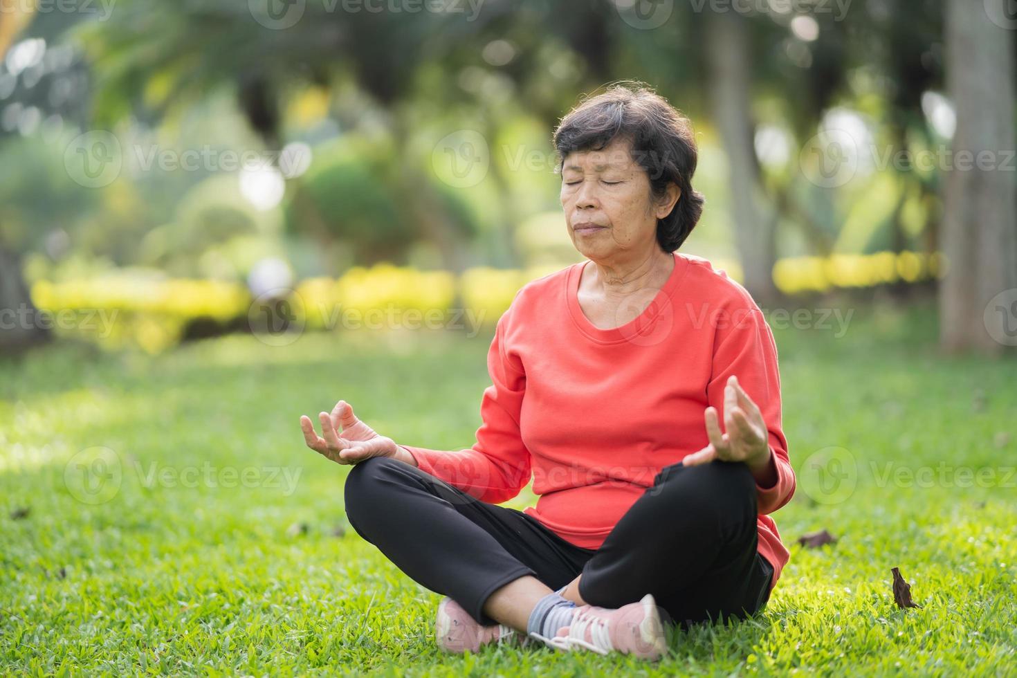donna asiatica anziana che pratica lezione di yoga, respira, medita in giardino. posa di mezzo loto con gesto mudra, allenamento, benessere, concetto di benessere foto