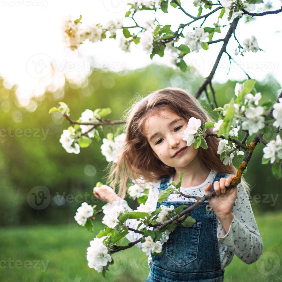 una graziosa bambina di 5 anni in un frutteto di mele bianco in fiore in primavera. primavera, frutteto, fioritura, allergia, profumo di primavera, tenerezza, cura della natura. ritratto foto