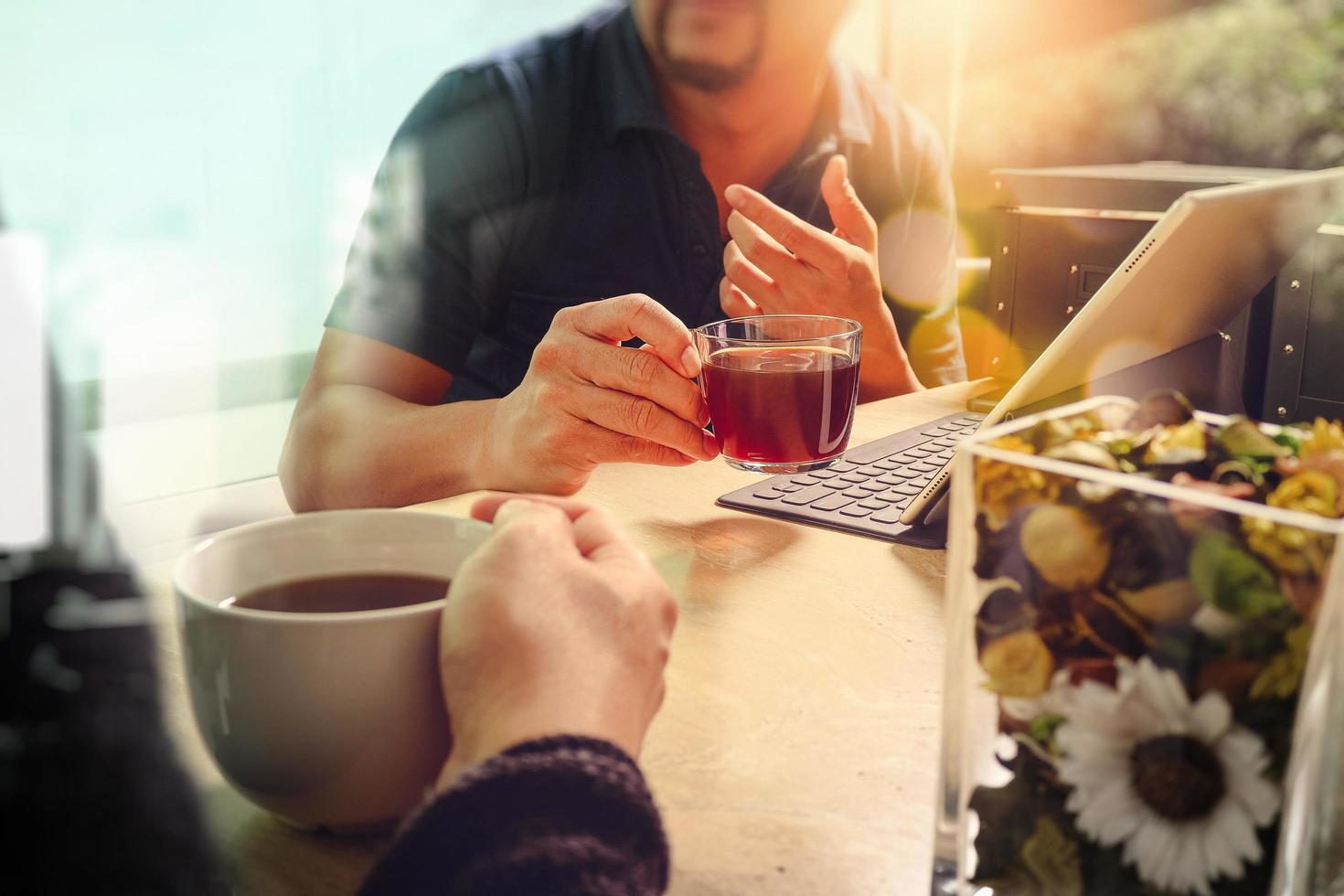 pausa caffè in ufficio con due colleghi designer seduti a chiacchierare davanti a tazze di caffè, vaso di fiori, docking station per tablet digitale tastiera intelligente su scrivania in marmo, film effetto filtri foto