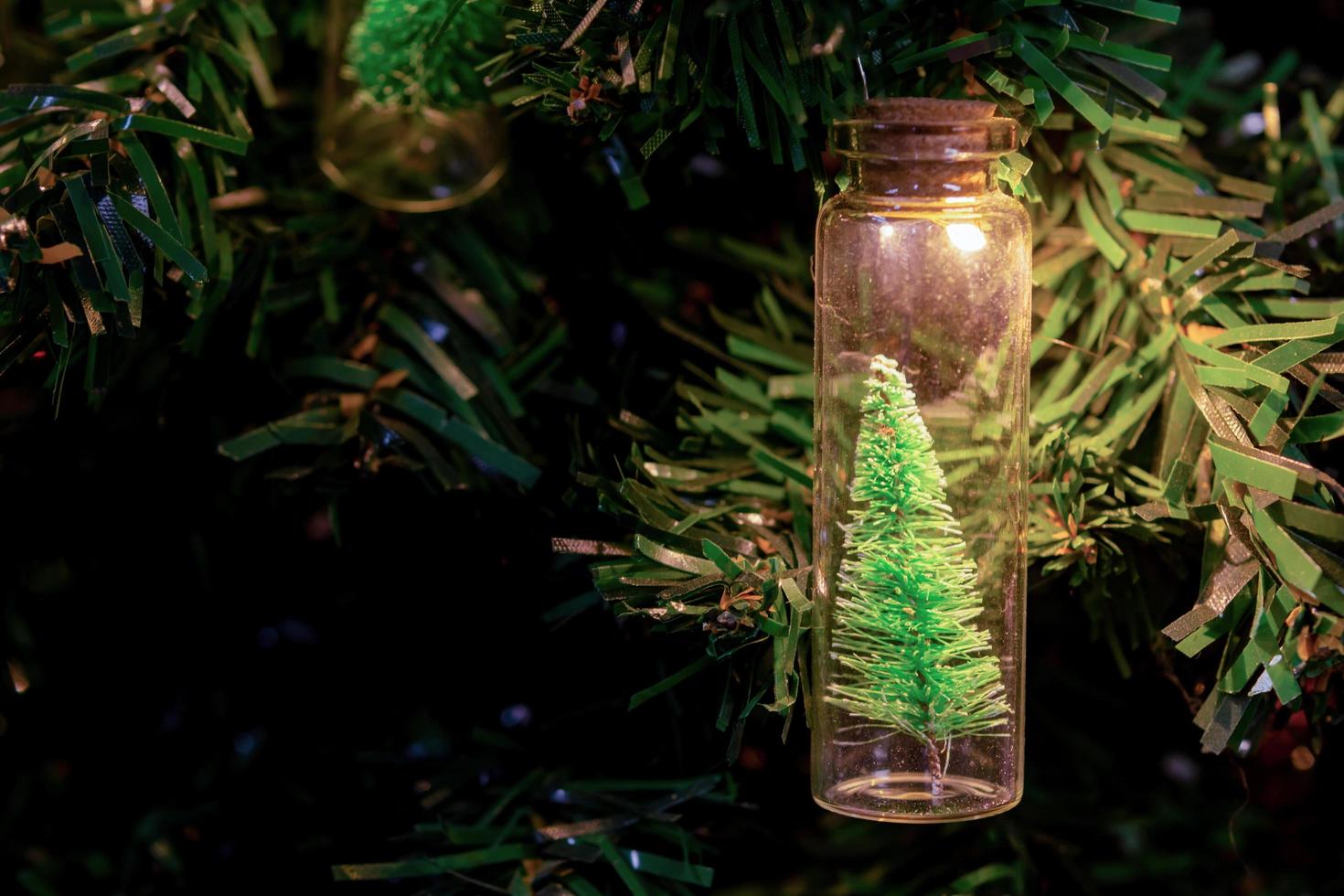 buon Natale e Felice Anno nuovo. appeso piccolo albero di natale in barattolo di vetro su rami di pino ghirlanda di albero di natale e ornamenti su bokeh astratto foto