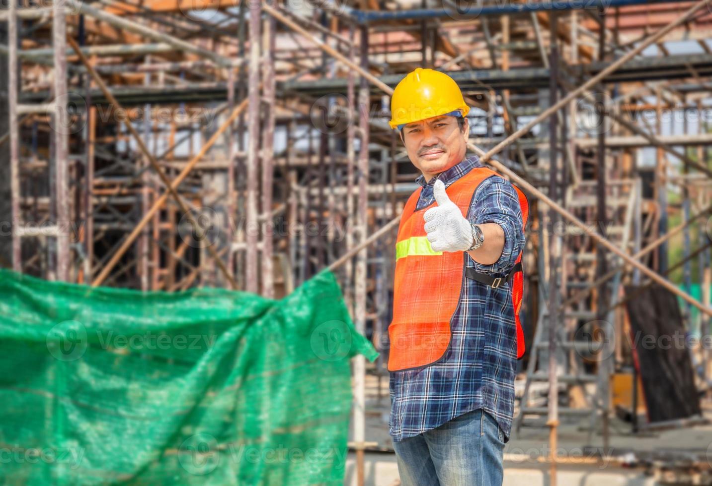 lavoratore uomo in elmetto in piedi con il pollice in su sopra il cantiere sfocato, concetto di successo foto