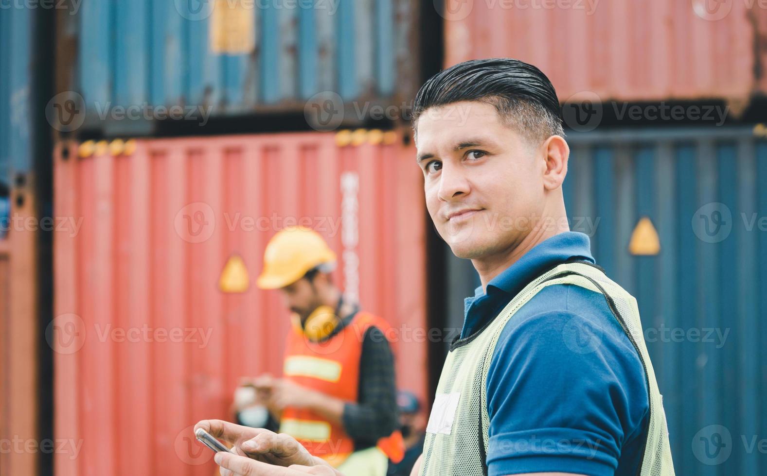 l'uomo dell'ingegnere utilizza il telefono cellulare, un lavoratore industriale che utilizza lo smartphone mobile nel carico di container industriali foto