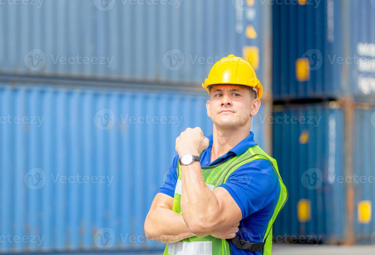 felicità caposquadra lavoratore in elmetto protettivo mostra forti muscoli del braccio al carico di container foto