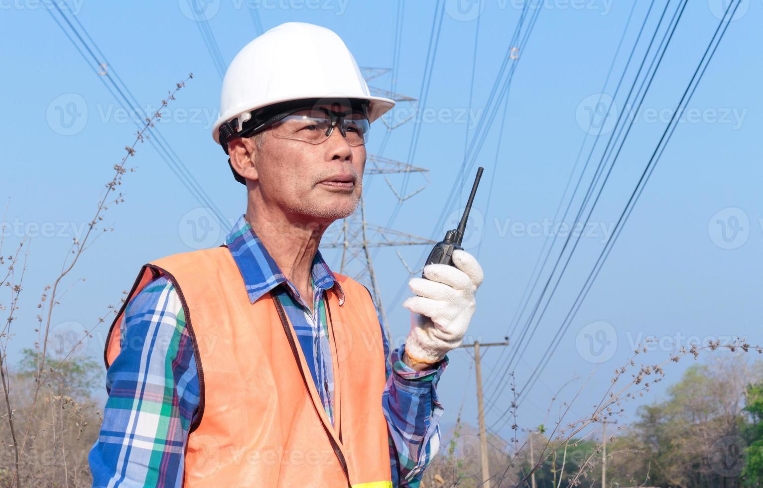 elettricista vicino alla linea di trasmissione un elettricista gestisce il processo di costruzione di una linea di trasmissione. meccanico in casco e riflettore e trasmettitore radio al lavoro foto