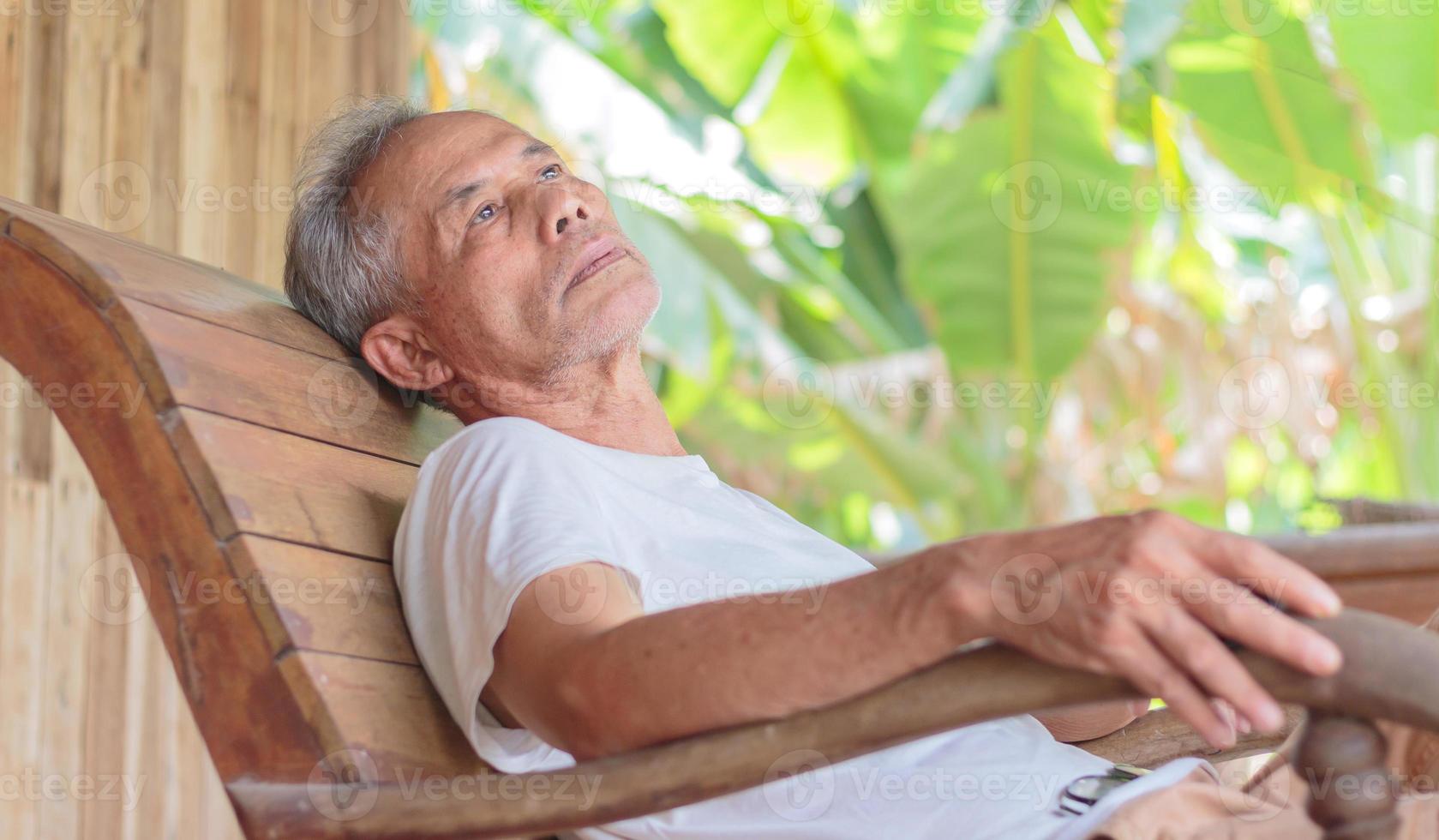 l'uomo anziano depresso si siede su una sedia a dondolo e pensa. pensionato deluso seduto su una sedia un vecchio malinconico sedeva da solo nella casa di cura con un'espressione triste sul viso. foto